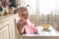 Sad funny naughty baby eating alone in the high chair