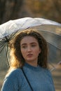 Sad girl with blue eyes and curly hair under transparent umbrella. Portrait of young woman in blue sweater Royalty Free Stock Photo