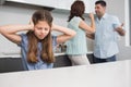 Sad girl covering ears while parents quarreling in kitchen