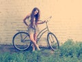Sad girl with her urban bike standing near white wall and looking down at feet, retro looking instagram toned shot