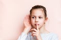 Sad girl holding her finger in front of her lips and hand near her ear listening. Call for silence Royalty Free Stock Photo