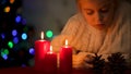 Sad girl playing with pine cone near burning candles, Christmas time magic