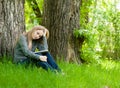 Sad girl sitting on grass and reading a book Royalty Free Stock Photo