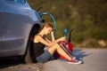 Sad girl sitting on the ground next to electric car. Holding charging cable and red gassoline canister Royalty Free Stock Photo