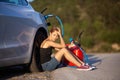 Sad girl sitting on the ground next to electric car. Holding charging cable and red gassoline canister Royalty Free Stock Photo