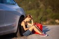 Sad girl sitting on the ground next to electric car with red gassoline canister. Holding phone Royalty Free Stock Photo