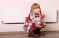 Sad girl sitting near heater. Children problem. Royalty Free Stock Photo