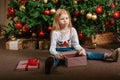 A sad girl is sitting next to a Christmas tree who received an unwanted gift on Christmas Day Royalty Free Stock Photo