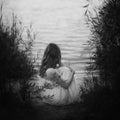 Sad girl sitting on sandy beach at sunset light near lake. back Royalty Free Stock Photo