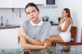 Sad girl sitting at table after conflict, woman friend on backround