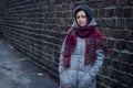 Sad girl stands near a brick wall in jacket hat and scarf Royalty Free Stock Photo