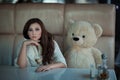 Sad girl at the table with a toy bear. Royalty Free Stock Photo