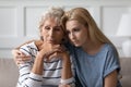 Sad grownup daughter sitting on sofa hugging desperate elderly mother