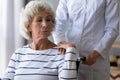 Sad handicapped woman sitting in wheelchair holding hand of caregiver