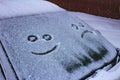 The sad and the happy smile on the snowy windshield of a car