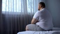 Sad heavy man sitting on bed at home, health problem, depression, insecurities Royalty Free Stock Photo