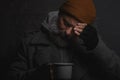 Sad homeless man with a gray beard holding a cup of hot tea to warm himself on a cold night Royalty Free Stock Photo