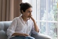 Sad Indian woman sit on armchair looks concerned, feels confused