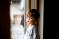 Sad kid looking out the window. Reflection in window glass. Face of two years old boy. Alone child. Little migrant child Royalty Free Stock Photo