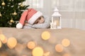 Sad kid in a striped cap lies at the Christmas tree