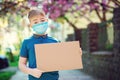 Sad kid wearing protective mask. Boy showing empty blank. Cute boy holding empty board outdoors. World global pandemic.