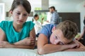 Sad kids leaning on sofa while parents arguing in background