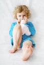 Sad little blonde curly sitting girl on the white with toy