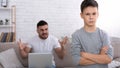 Sad little boy looking at camera, angry father with laptop yelling at him