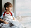A sick child sits near the window and looks at the sea Royalty Free Stock Photo