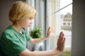 Sad little boy is sitting near window and watching street. Lonely at home. No friends, no siblings. One baby in family. Child Royalty Free Stock Photo