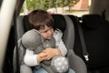 Sad little boy with toy sitting in safety seat alone inside car Royalty Free Stock Photo