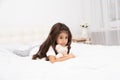 Sad little brunette girl lying with teddy bear on bed at home