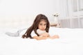 Sad little brunette girl lying with teddy bear on bed at home