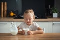 Sad little caucasian girl refuses to drink milk in the stylish kitchen