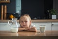 Sad little caucasian girl refuses to drink milk in the stylish kitchen