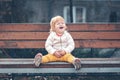 A sad little child is sitting on a bench on the playground alone. Rainy weather. The concept of lost childrens Royalty Free Stock Photo
