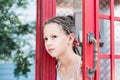 A sad little girl with afro-braids looks out from an old English telephone booth. Generational contrast Royalty Free Stock Photo