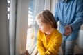 Sad little girl with Down syndrome looking throug window with her father at background. Royalty Free Stock Photo