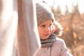 Sad little girl in a hat and a scarf on a walk in the autumn park holds the hand of a parent Royalty Free Stock Photo