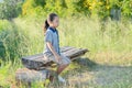 Sad little girl sitting alone outside on a bench in park depressed. Serious child girl sitting alone in summer park. Concept of Royalty Free Stock Photo