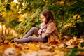 Sad little girl sitting on ground in fallen leaves. children`s resentment