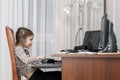 Sad little girl sitting at her dad computer and looking at screen while doing her homework. Tired kid doing homework at home. Royalty Free Stock Photo