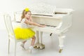 Sad little girl sitting leaning on a white Grand piano. Royalty Free Stock Photo