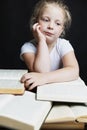 Sad little girl sitting with a pile of books. Knowledge and education. Black background. Vertical Royalty Free Stock Photo