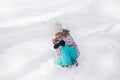 Sad little girl sitting in a snowy forest in the winter and crying, her clothes stained with snow