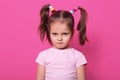 Sad little girl stands against pink wall, looks at camera. Cute kid wears rose t shirt, has two fanny poni tails with many Royalty Free Stock Photo