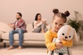 Sad little girl with toy and her arguing parents on sofa in living room