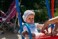 Sad, little girl in a white dress and hat, riding on a swing, summer sun and heat. playground. childhood, serenity Royalty Free Stock Photo