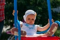 Sad, little girl in a white dress and hat, riding on a swing, summer sun and heat. playground. childhood, serenity. negative Royalty Free Stock Photo