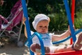 Sad, little girl in a white dress and hat, riding on a swing, summer sun and heat. playground. childhood, serenity. negative Royalty Free Stock Photo